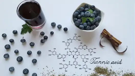 Blueberries on a table next to a glass of blueberry juice, a bowl of blueberries and a chemical formular