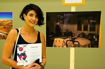 The winner of the competition with her Certificate in her hand next to her photography