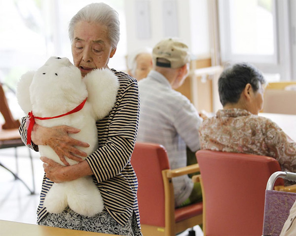 Old Woman hugging a Teddybear with three people sitting in the background